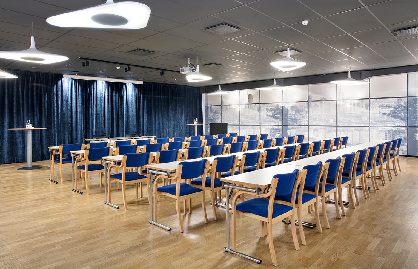 Konferensrum med vita långa bord, trästolar med blå dynor, blå gardiner, vita lampor i taket