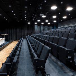Aula med mörka uppfällda tygstolar, spotlights i taket