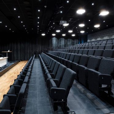 Stor aula med uppfällda grå stolar, spotlights i taket