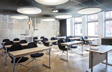Konferensrum med träbord, grå stolar, vita lampor i taket